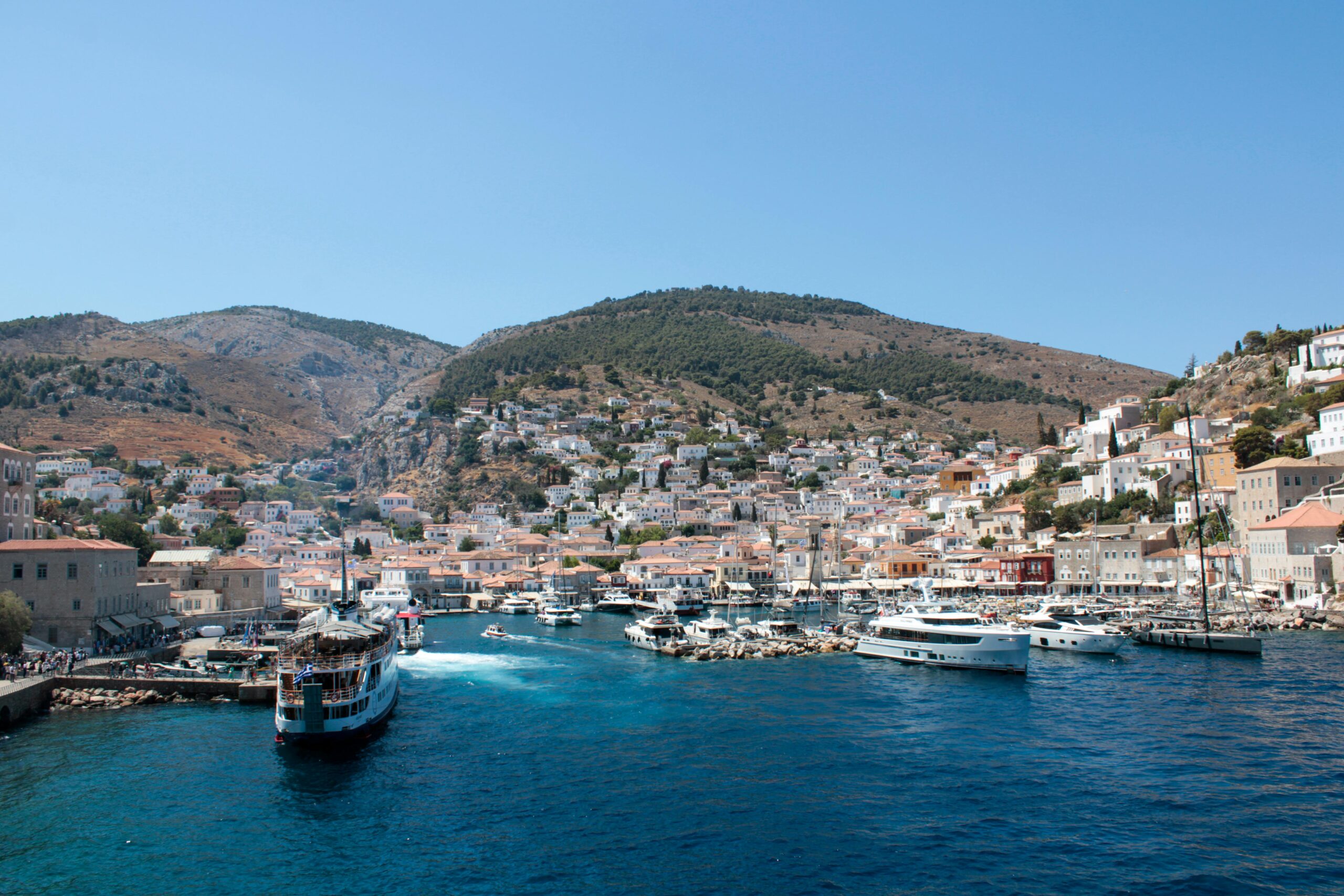 A vibrant view of Hydra Island's picturesque harbor with boats and buildings under a clear blue sky.