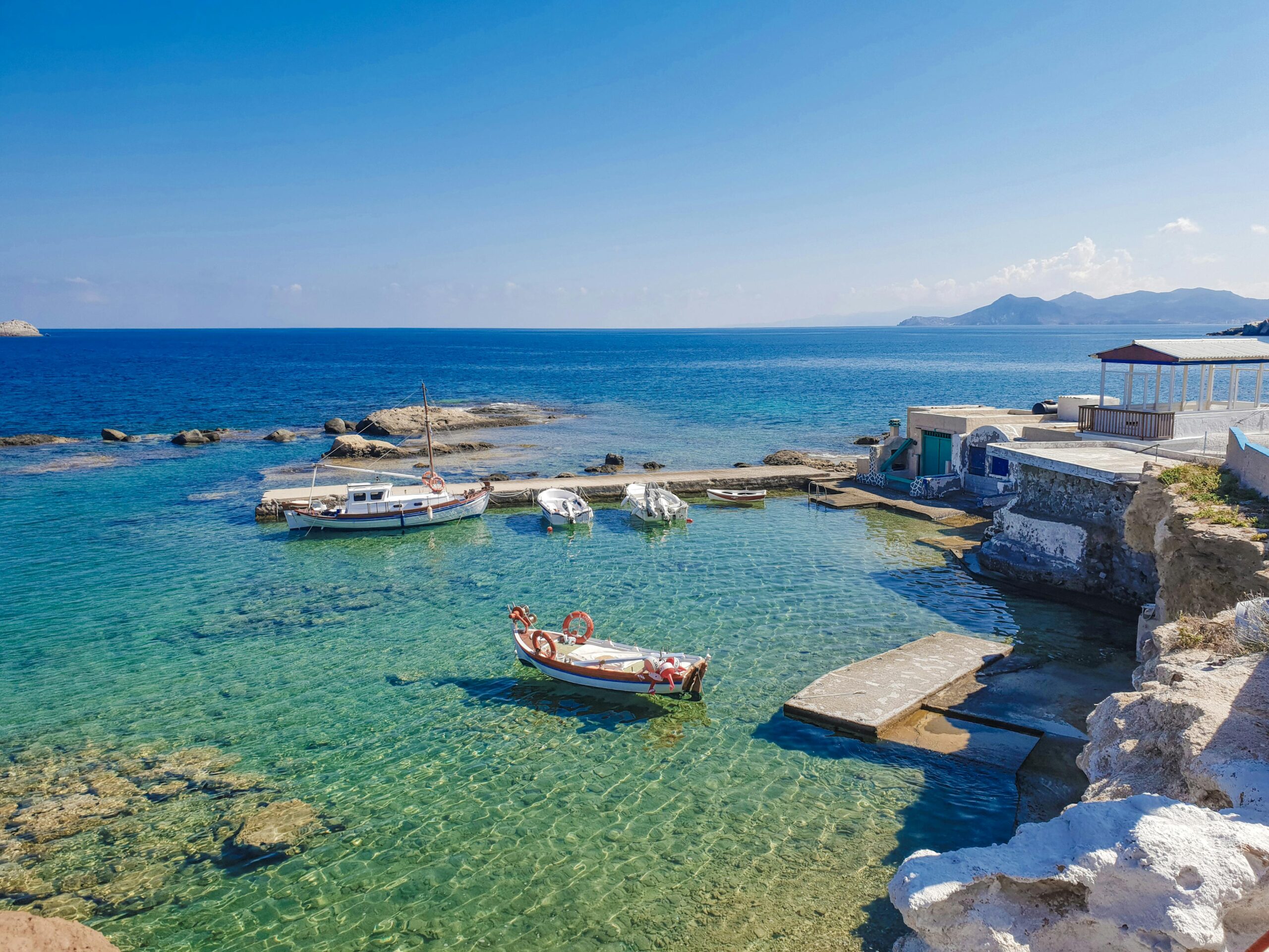 Peaceful harbor scene with boats moored in crystal-clear waters, showcasing Cycladic architecture.